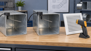 Two air-temperature probes extend into separate metal duct sections beside an infrared thermometer aimed at a white grille.