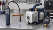 An electronic leak detector beside a vacuum pump and digital vacuum gauge on a workbench.