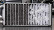 Automotive evaporator core with frost bridging part of its fins beside an unfrosted section, illustrating how ice can obstruct airflow.