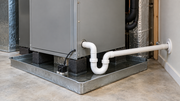 Indoor air handler above an auxiliary drain pan, with a white condensate drain pipe and an overflow safety switch.